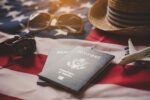 A close-up photograph of two U.S. passports, a U.S. flag, sunglasses, a straw hat, and a toy airplane, illustrating the final steps of preparing for travel after learning how to fill out a DS-82 form PDF for renewal.