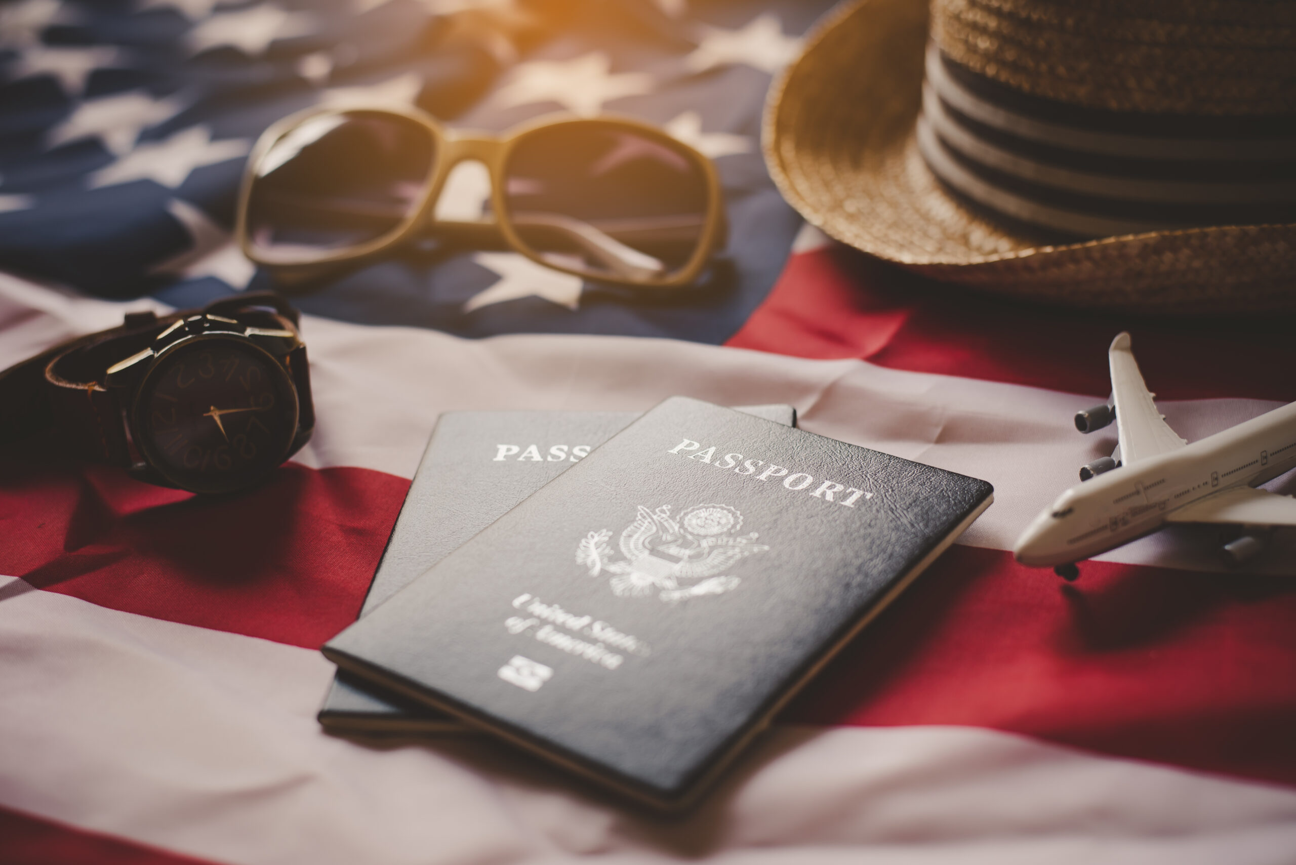 A close-up photograph of two U.S. passports, a U.S. flag, sunglasses, a straw hat, and a toy airplane, illustrating the final steps of preparing for travel after learning how to fill out a DS-82 form PDF for renewal.